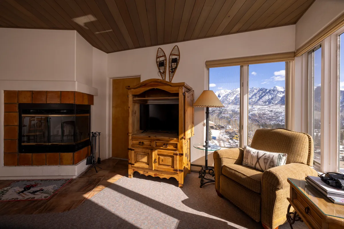 A spacious living room with a fireplace, television cabinet, armchair, and large windows framing mountain views. The environment is warm and comfortable, ideal for relaxing after a day of adventure or hosting group gatherings.