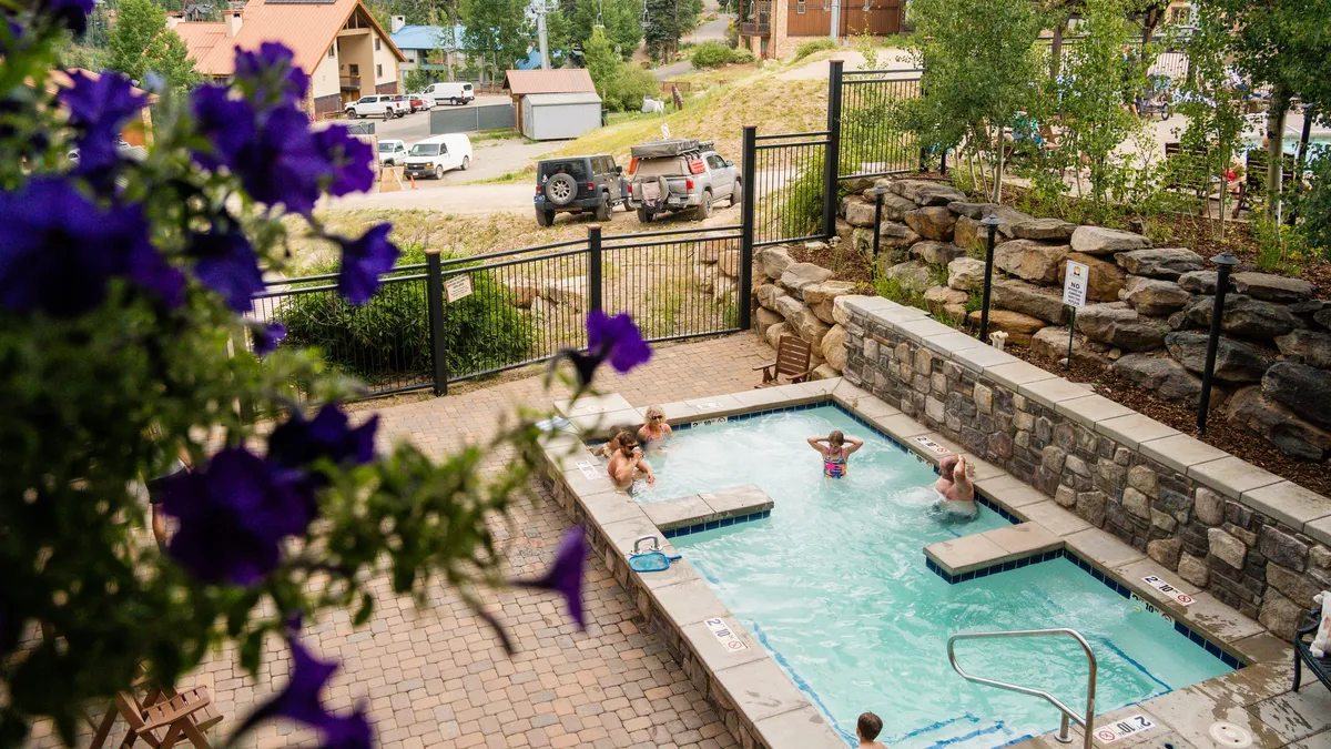 An exterior shot of a swimming pool bordered by lush flowers, with people enjoying the water and socializing. The atmosphere is lively and cheerful, reflecting the fun and relaxation offered by the resort pool.