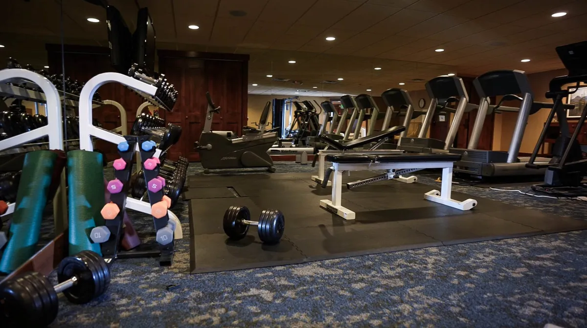 A well-equipped fitness center featuring treadmills, dumbbells, and a weight bench. Large windows allow natural light to fill the space, creating an energizing atmosphere for workouts and group fitness activities.