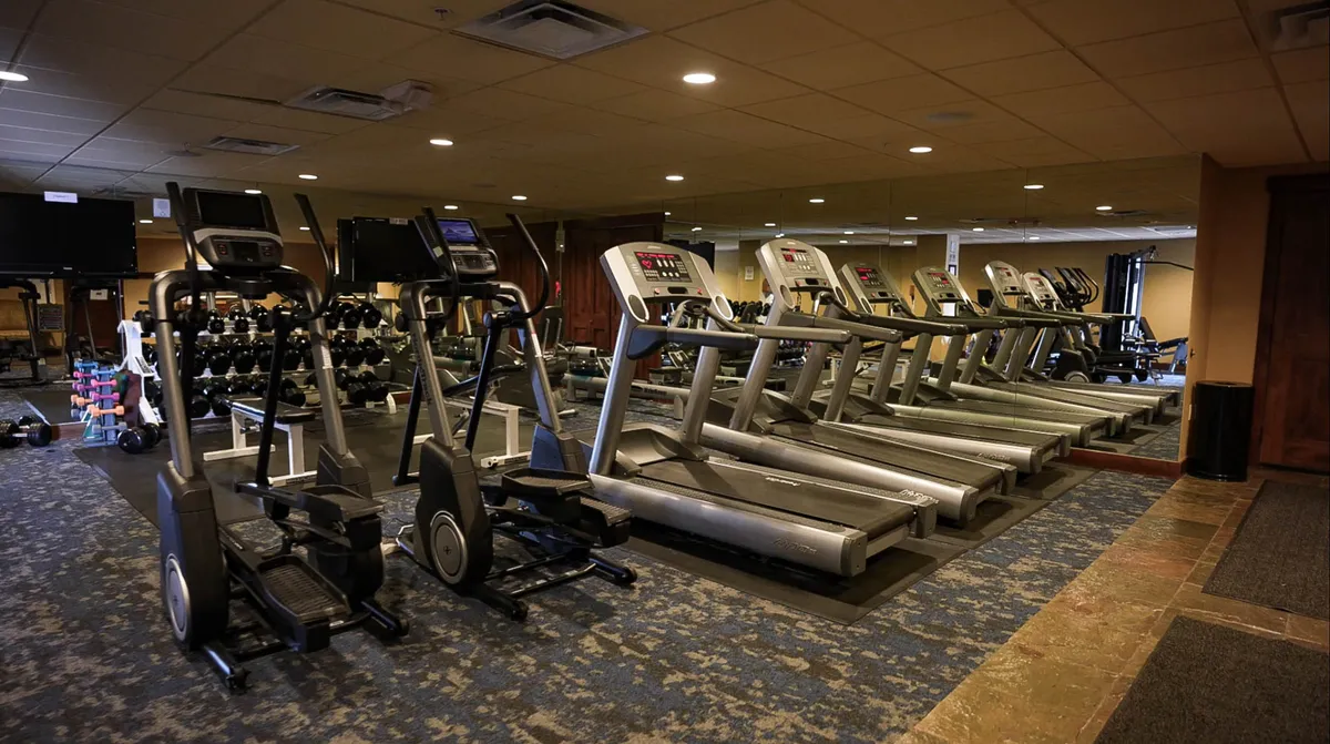 An interior fitness center is depicted here, featuring treadmills, elliptical machines, dumbbells, and plenty of mirrors. The space looks modern, bright, and motivational, ideal for personal workouts or group exercise.