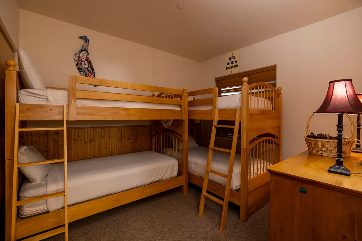 A cozy guest bedroom equipped with wooden twin bunk beds, artistic wall decor, a decorative lamp, and inviting furnishings. The playful yet relaxing atmosphere suggests a space perfect for children or groups to unwind and share fun moments.