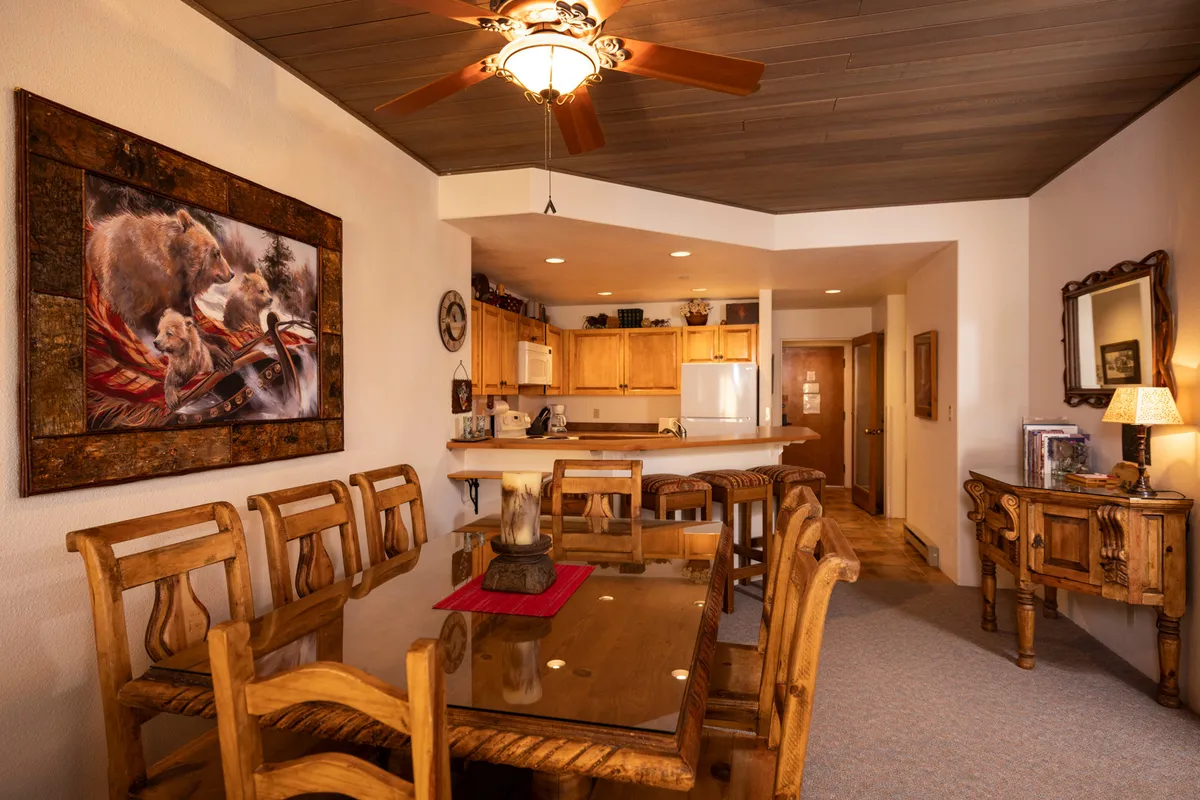 A warm and inviting dining area featuring a rustic wooden dining table, wooden furniture, and a charming bear painting on the wall. The space is brightened by natural light, providing a cozy setting for shared meals and meaningful conversations.